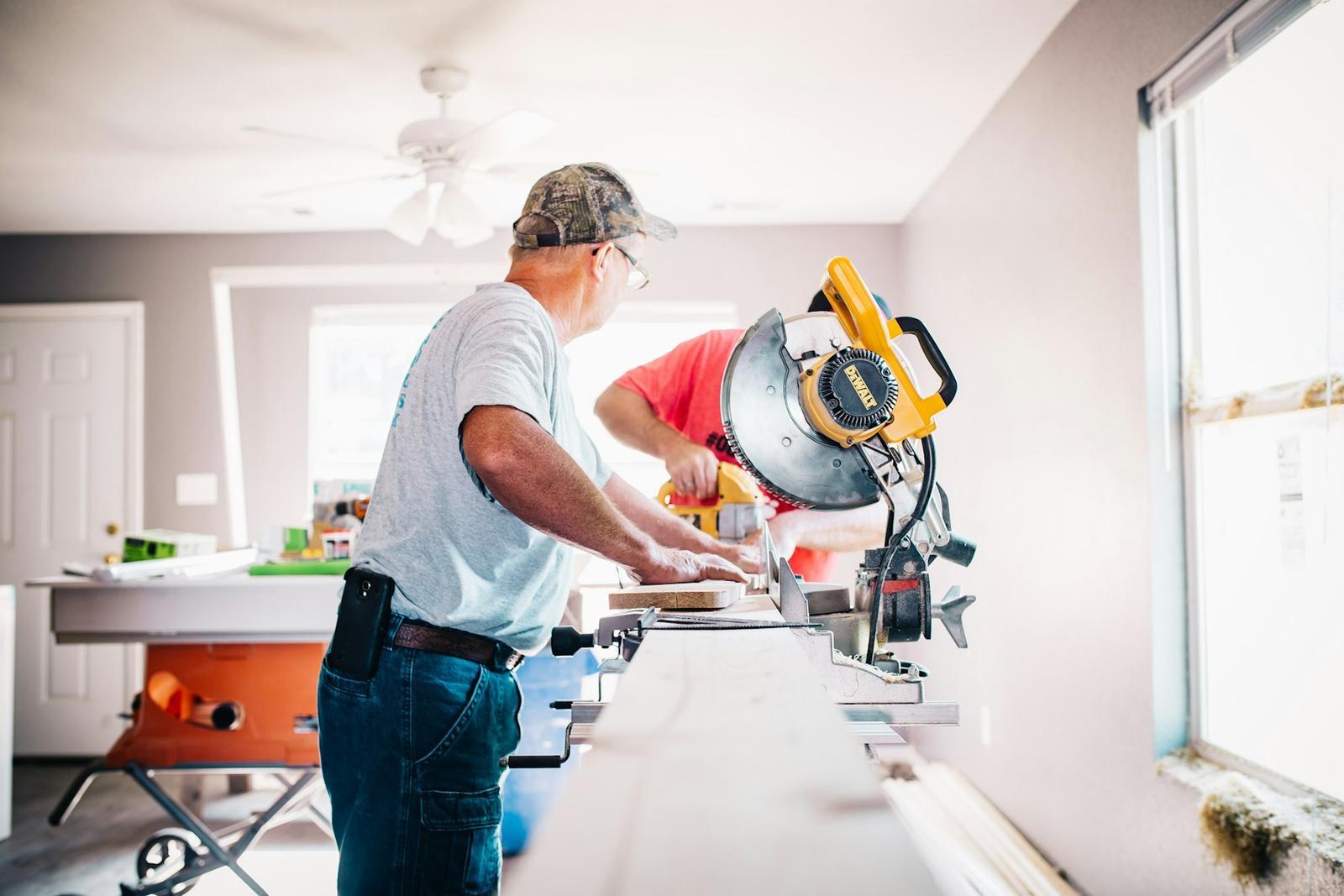 Two carpenters cutting trim inside a house during a remodel